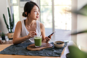 tè matcha ragazza che mescola nel bicchiere seduta al tavolo con telefono